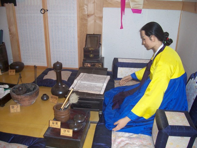 A scribe at work in a room filled with pottery vessels.