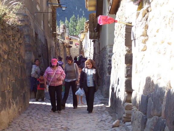 Ancient street between ancient walls still housing residents; a red-wrapped broom sticking out over a doorway means beer is available; Ollantaytambo